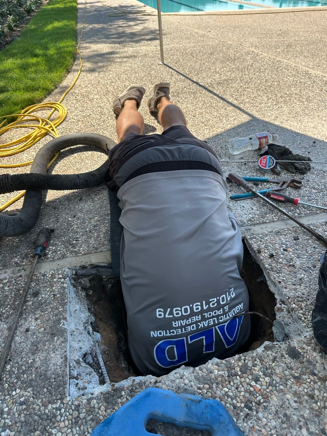 An Aquatic Leak Detection technician repairing pool plumbing in a deck trench